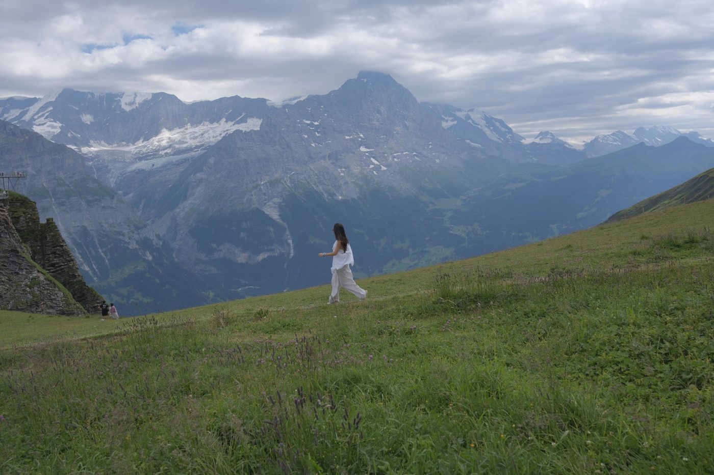 Michelle walking across an alpine meadow with snow-capped mountains behind